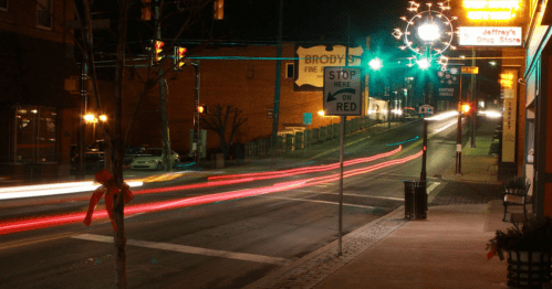 A quiet street at night with light trails from passing cars, decorated with holiday lights and a stop sign.