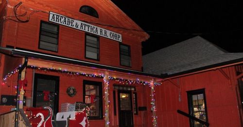 A brightly lit orange building with a sign reading "Arcade & Attica R.R. Corp." decorated for the holidays at night.