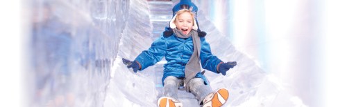 A joyful child in a blue coat slides down an icy slide, smiling with excitement.