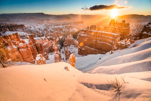 A stunning winter landscape at sunrise, showcasing snow-covered cliffs and rock formations in a canyon.