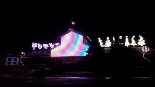 Colorful holiday lights decorate a building at night, featuring festive designs like trees and snowmen.