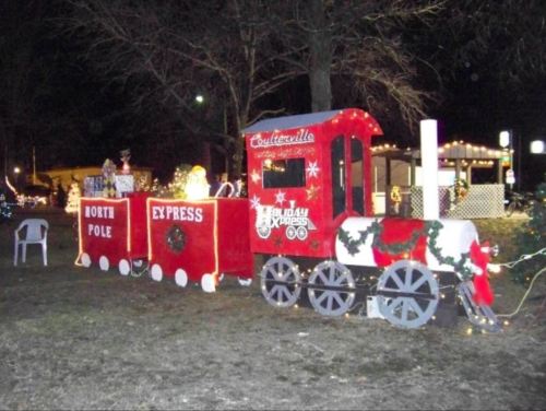 A festive train display decorated for the holidays, featuring "North Pole Express" and colorful lights at night.