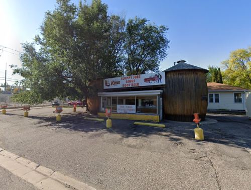A rustic building with a round wooden structure, featuring a sign for "Sloppy Joe's Rings & Root Beer" and outdoor seating.