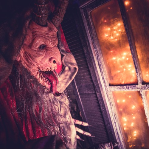 A menacing creature with horns and a long tongue, set against a window with warm, glowing lights outside.