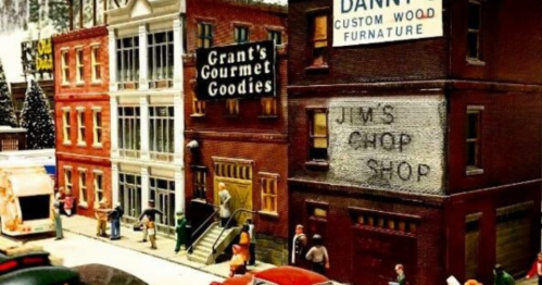 A miniature street scene featuring shops, people, and vintage cars, showcasing detailed model buildings and signage.