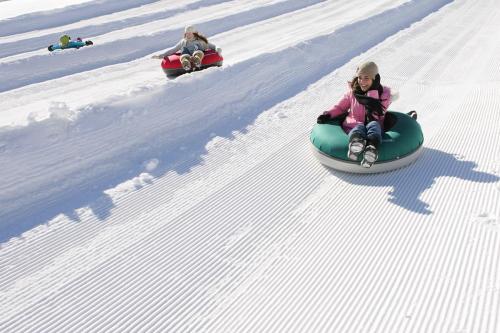 Three children are tubing down a snowy slope, enjoying a winter day in bright winter gear.