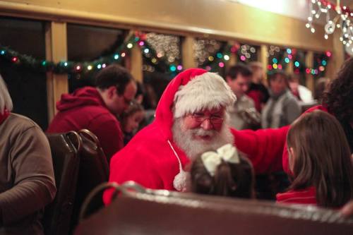 A joyful Santa Claus in a red suit interacts with children in a festive, decorated setting.