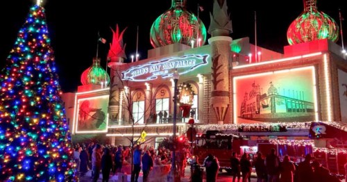 A festive scene featuring a brightly lit building with colorful decorations and a large Christmas tree in the foreground.