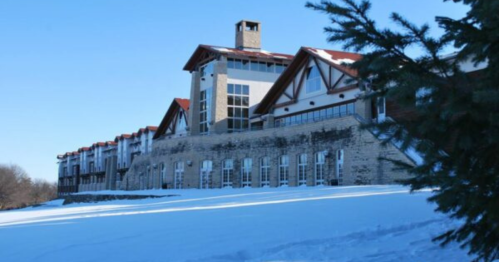 A large, modern building with a stone base and red roof, surrounded by snow and trees under a clear blue sky.