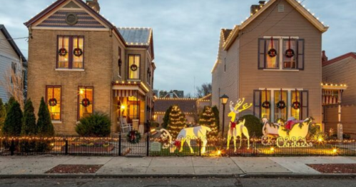 Two festive houses decorated with Christmas lights and holiday decorations, including reindeer and a sleigh in the yard.