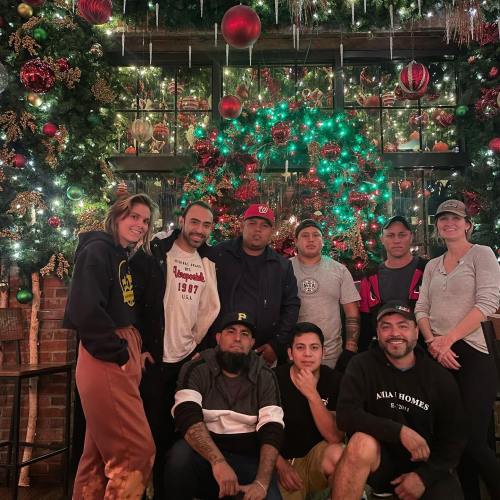 A group of nine people poses together in front of a festive, decorated Christmas tree and holiday backdrop.