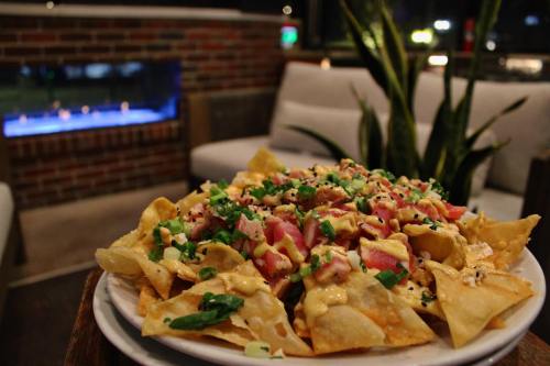 A plate of nachos topped with cheese, diced tomatoes, and green onions, set against a cozy indoor backdrop.