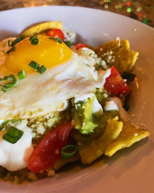 A plate of chilaquiles topped with a fried egg, diced tomatoes, green onions, and drizzled with cream.