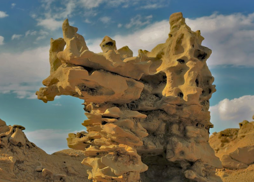 A unique rock formation with intricate shapes against a blue sky and scattered clouds.