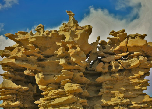 Unique rock formation with layered, textured structures against a blue sky and wispy clouds.