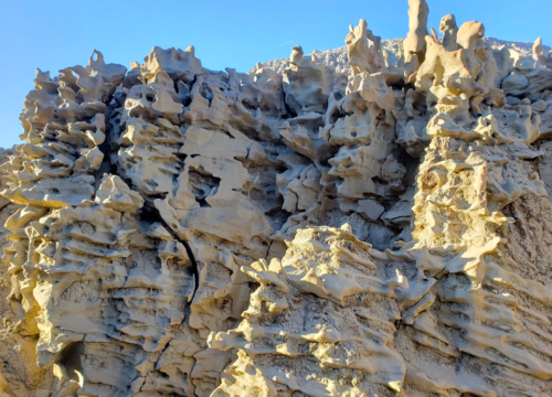Textured rock formation with intricate, jagged shapes and a light sandy color against a clear blue sky.
