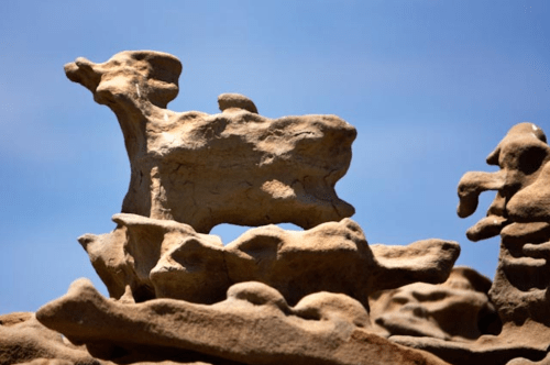 A rock formation resembling a dog stands against a clear blue sky.