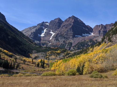 Scenic mountain landscape with snow-capped peaks and vibrant autumn foliage in a valley under a clear blue sky.