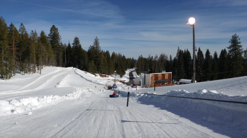 A snowy landscape with a tubing hill, trees in the background, and a clear blue sky.