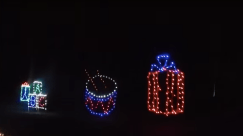Colorful holiday lights display featuring a drum, a gift box, and wrapped presents against a dark background.