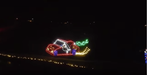 A colorful light display of a car with a green wreath, set against a dark night sky.