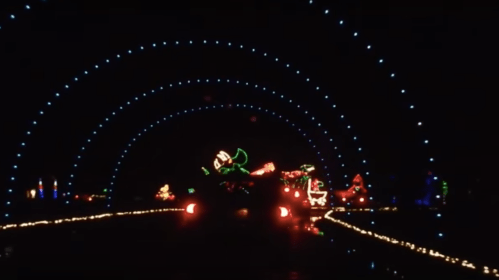 Colorful holiday lights create an archway effect in a dark setting, featuring festive decorations and glowing displays.