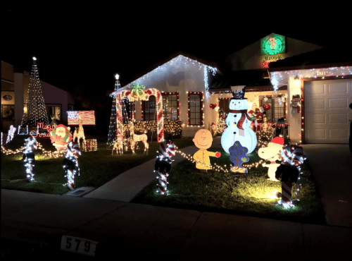 A festive house decorated with colorful Christmas lights, featuring snowmen, cartoon characters, and holiday displays.