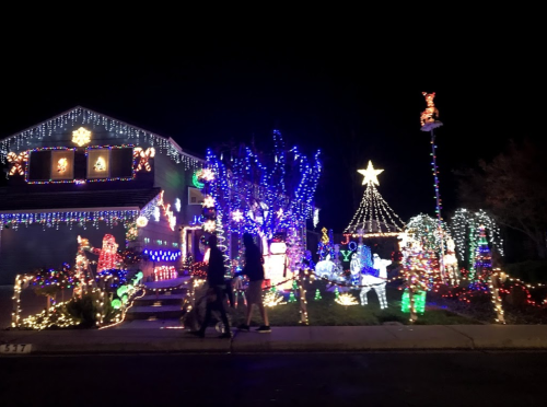 A brightly lit house decorated with colorful Christmas lights and festive displays, with two people walking by.