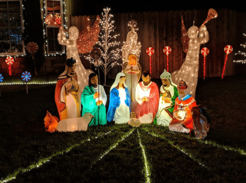 A colorful nativity scene with illuminated figures of Mary, Joseph, and baby Jesus, surrounded by festive decorations.