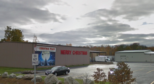 A building labeled "Merry Christmas" and "Christmas Place" with a cloudy sky and parked cars nearby.