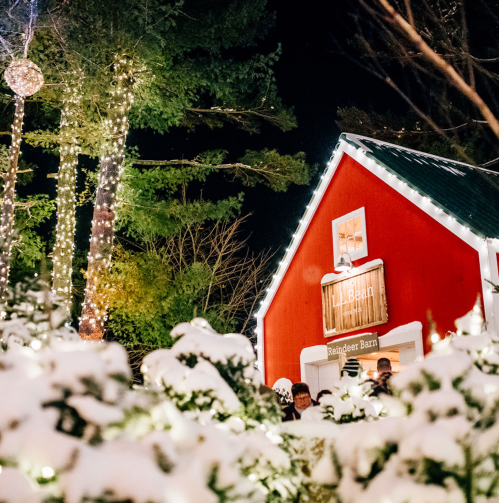 A cozy red barn adorned with holiday lights, surrounded by snow-covered trees and festive decorations at night.