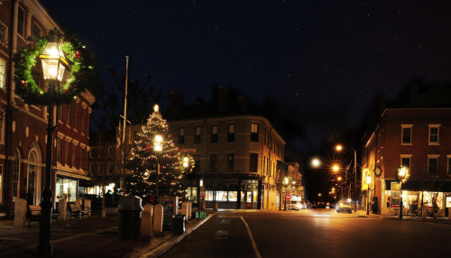 A charming town square at night, adorned with festive lights and a decorated Christmas tree, under a starry sky.