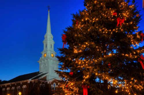 A decorated Christmas tree in front of a church steeple, illuminated against a twilight sky.