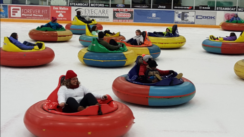 People enjoying a fun game of bumper cars on ice, sitting in colorful inflatable tubes on a rink.