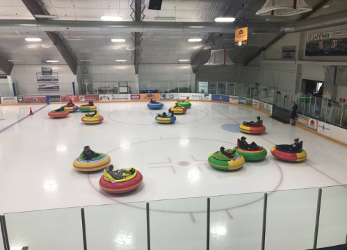 Aerial view of people enjoying bumper cars on ice, surrounded by colorful inflatable rings in an ice rink.