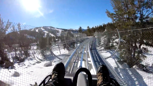 View from a roller coaster track winding through snowy mountains, with a clear blue sky above.