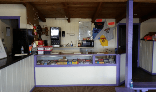 A small concession stand with a counter, soda machine, and various snacks displayed in a casual setting.