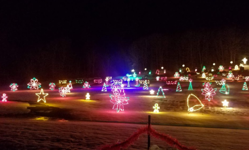 Colorful holiday lights illuminate a snowy landscape, featuring various festive shapes like trees, stars, and candy canes.