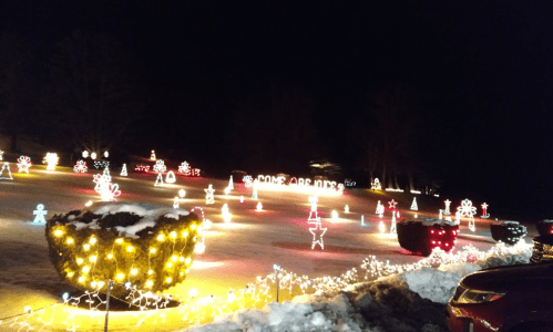 A festive display of colorful Christmas lights illuminating a snowy yard at night, featuring various holiday decorations.