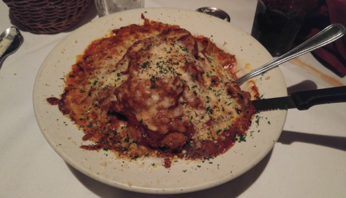 A plate of baked chicken parmesan topped with melted cheese and marinara sauce, garnished with parsley.