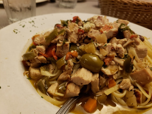 A plate of pasta topped with diced chicken, vegetables, and herbs, served with a spoon on a table.