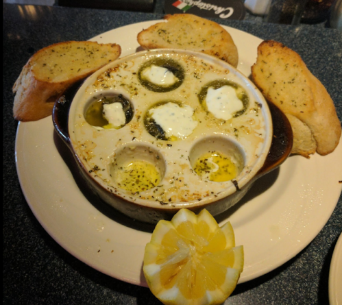 Baked dish with six stuffed mushrooms, garlic bread slices, and a lemon wedge on a plate.