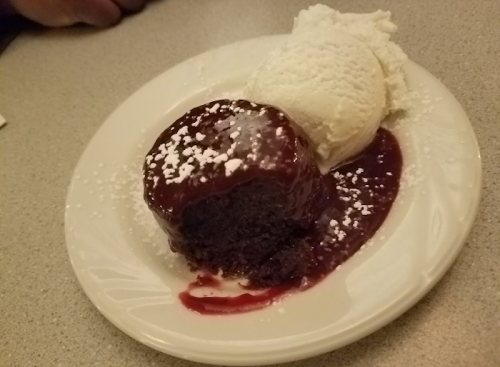 A chocolate dessert topped with berry sauce and powdered sugar, served with a scoop of vanilla ice cream.