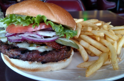 A juicy burger with lettuce, tomato, onion, and pickles, served with a side of crispy French fries.