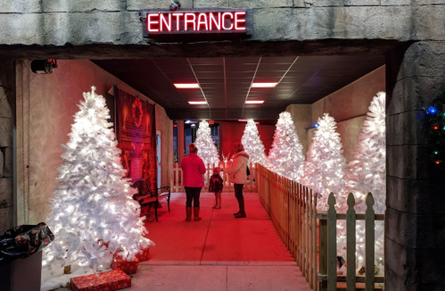 A festive entrance with glowing white Christmas trees and red lighting, featuring two people chatting.