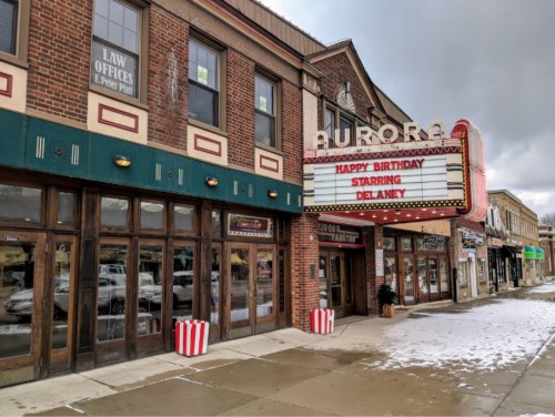 A vintage theater marquee displays "Happy Birthday Starring DeLanney" outside a brick building on a snowy street.