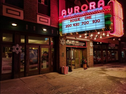 The Aurora Theatre entrance at night, featuring a marquee for "Rogue One" and festive decorations.