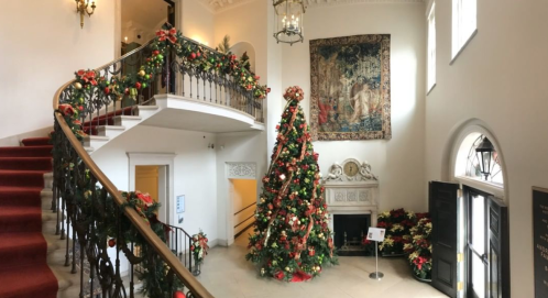 A festive staircase adorned with garlands and a large Christmas tree, surrounded by holiday decorations.