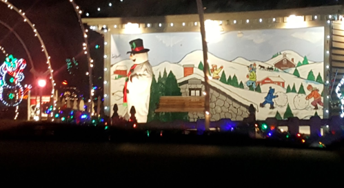 A festive mural featuring a snowman, snowy mountains, and playful animals, surrounded by colorful holiday lights.