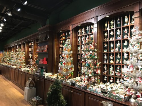 A festive store display featuring shelves filled with colorful ornaments and decorated Christmas trees.